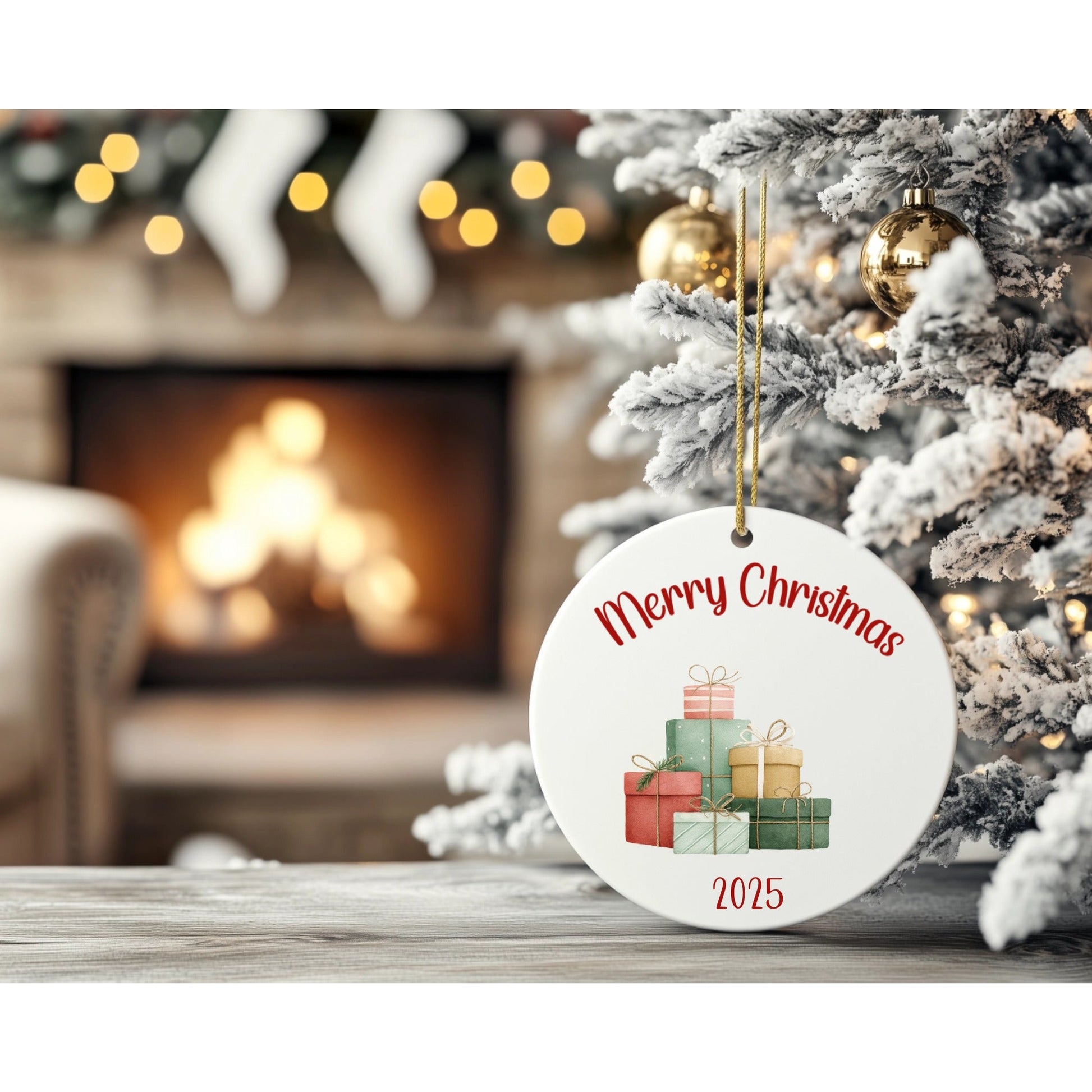 Christmas ornament with 'Merry Christmas 2025' text and gift illustrations, placed on a surface with a decorated tree and fireplace in the background.
